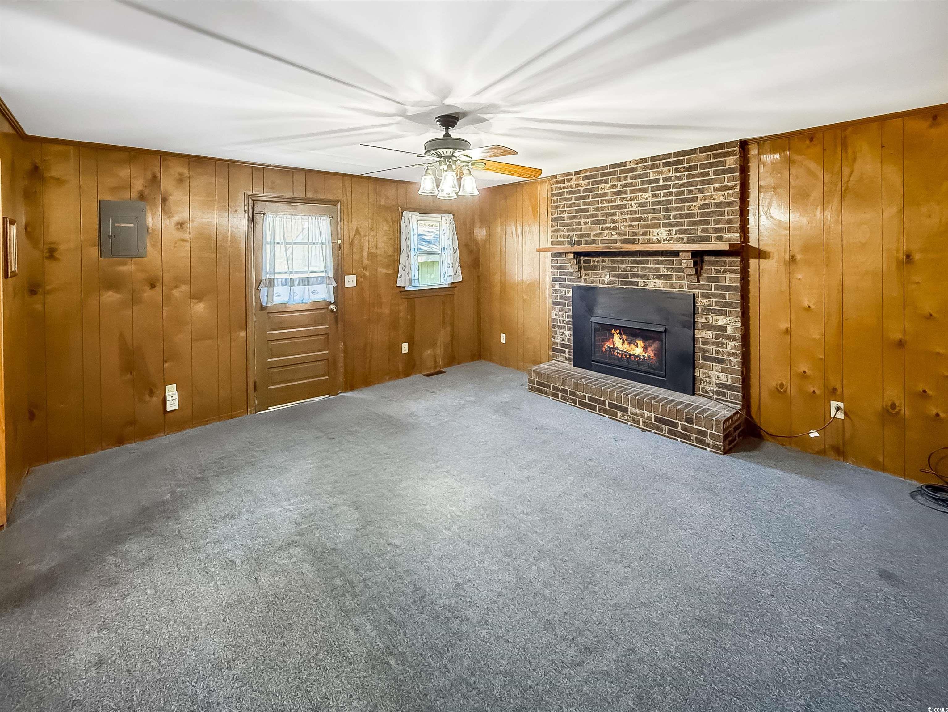 1682 Pickens Street Georgetown, SC 29440 - Photo 12 of 39 Unfurnished living room featuring a brick fireplace, carpet, wood walls, ceiling fan, and electric panel
