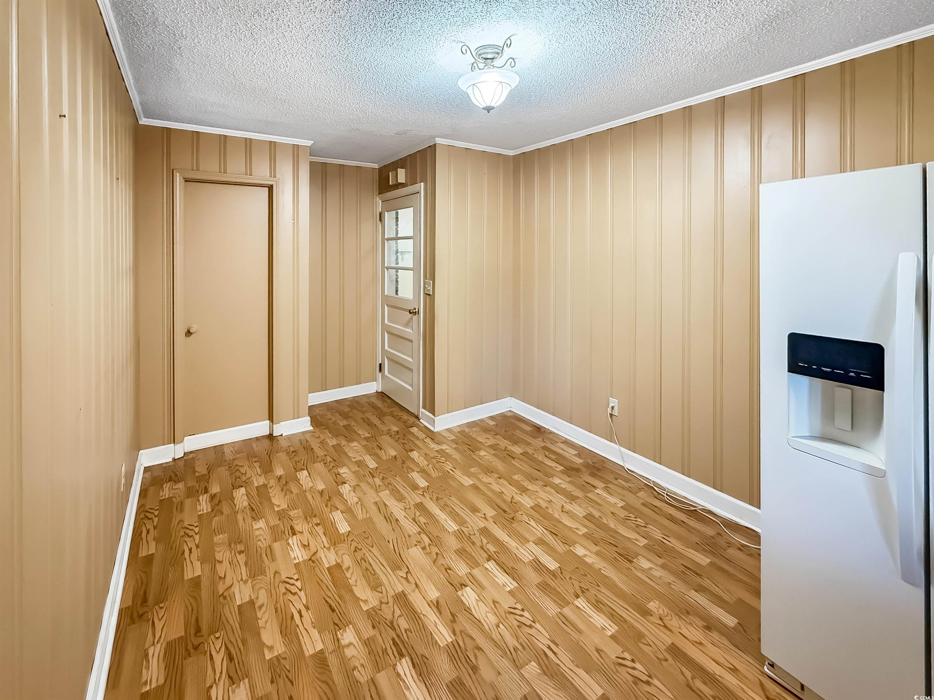 1682 Pickens Street Georgetown, SC 29440 - Photo 20 of 39 Unfurnished dining area featuring ornamental molding, light wood-style floors, a textured ceiling, and wooden walls