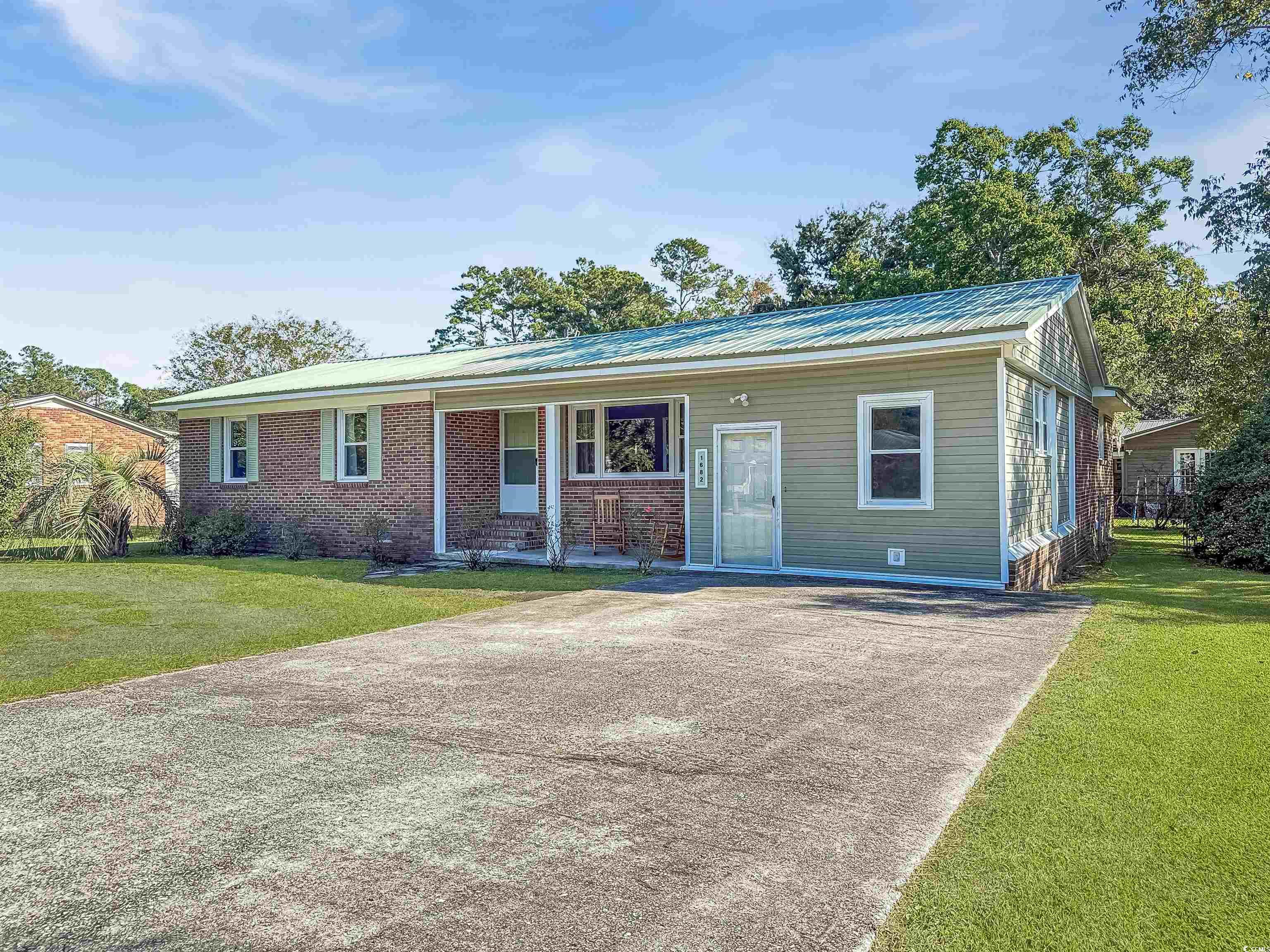 View of front facade with a front yard, brick siding, a metal roof, a porch, and concrete driveway