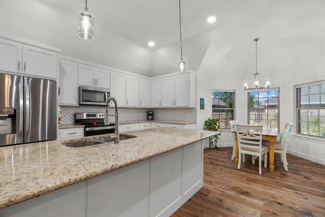 a kitchen with stainless steel appliances granite countertop a sink a stove a refrigerator cabinets and chairs