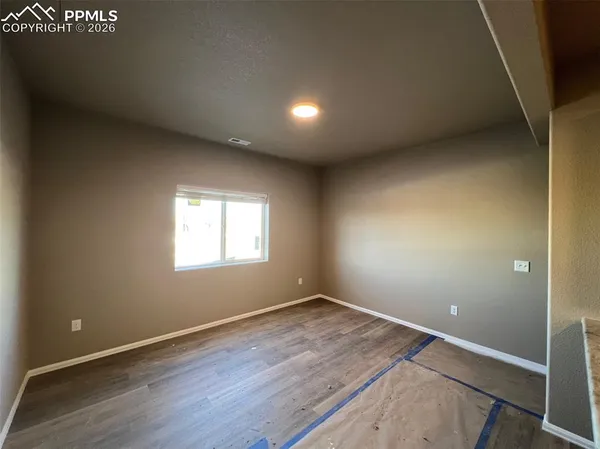 a view of an empty room and kitchen with wooden floor