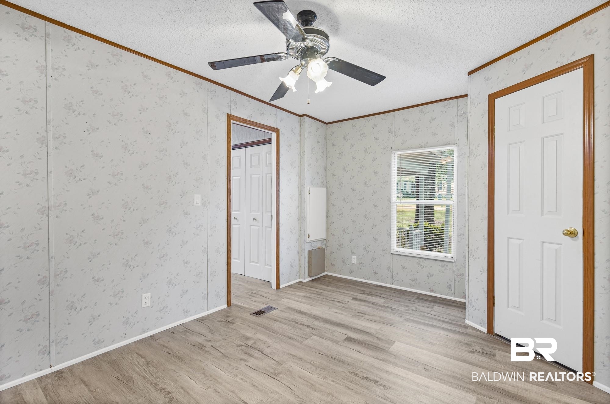 8675 Hunters Pointe Drive North Theodore, AL 36582 - Photo 11 of 20 Room featuring wood-finish flooring, patterned wall panels with wood trim, a ceiling fan with integrated lighting, and a white six-panel door with brass hardware