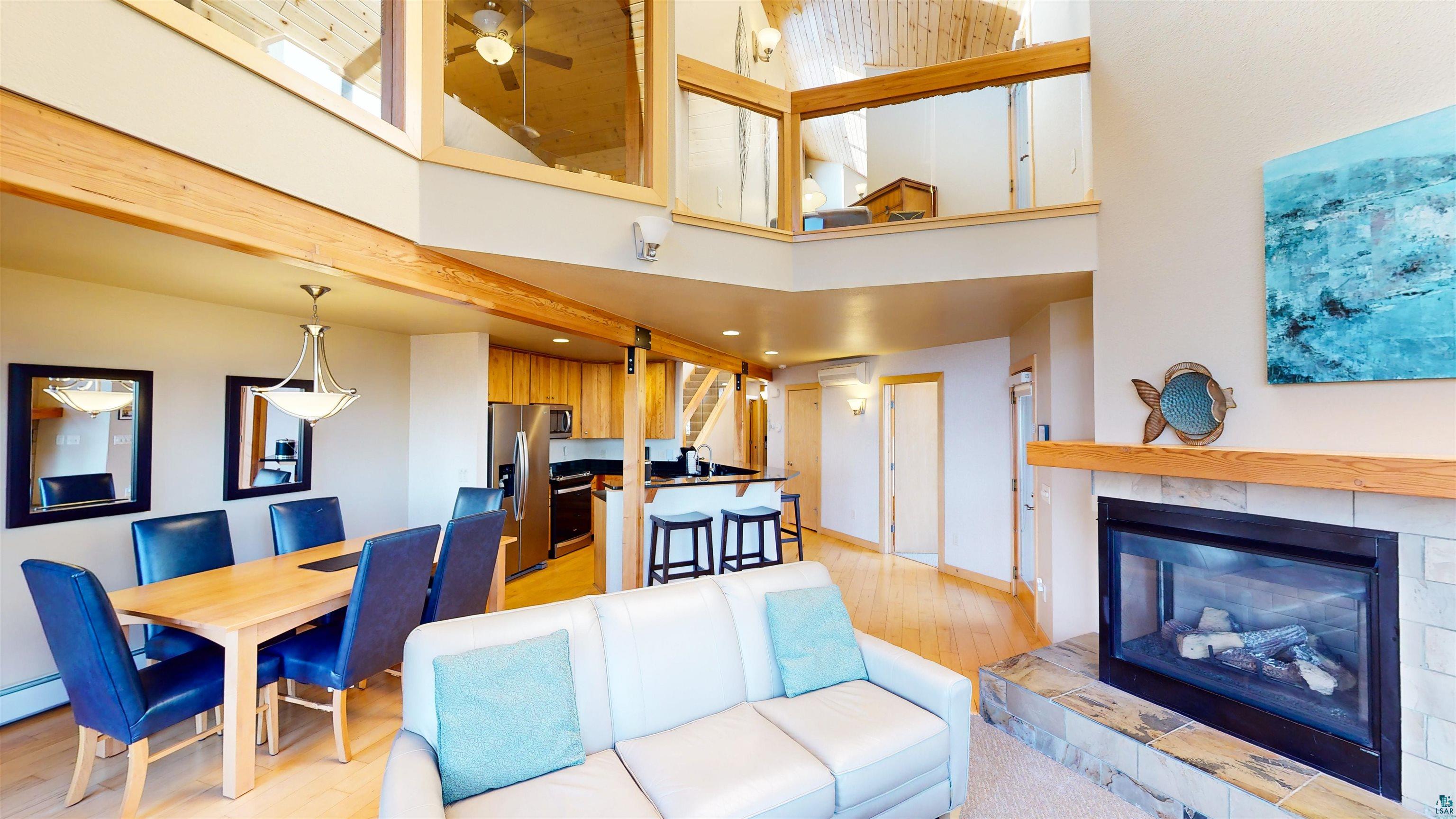 40 Surfside Drive, Unit 5D Tofte, MN 55615 - Photo 6 of 37 Open-concept living space featuring a stone-surround fireplace, light wood-finish flooring, a dining area with a modern chandelier, and a kitchen with stainless steel appliances and bar seating