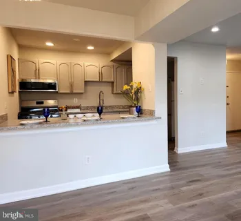 a kitchen with stainless steel appliances granite countertop a refrigerator a sink a stove a microwave and white cabinets with wooden floor