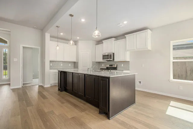 a kitchen with kitchen island granite countertop wooden floors white cabinets and stainless steel appliances