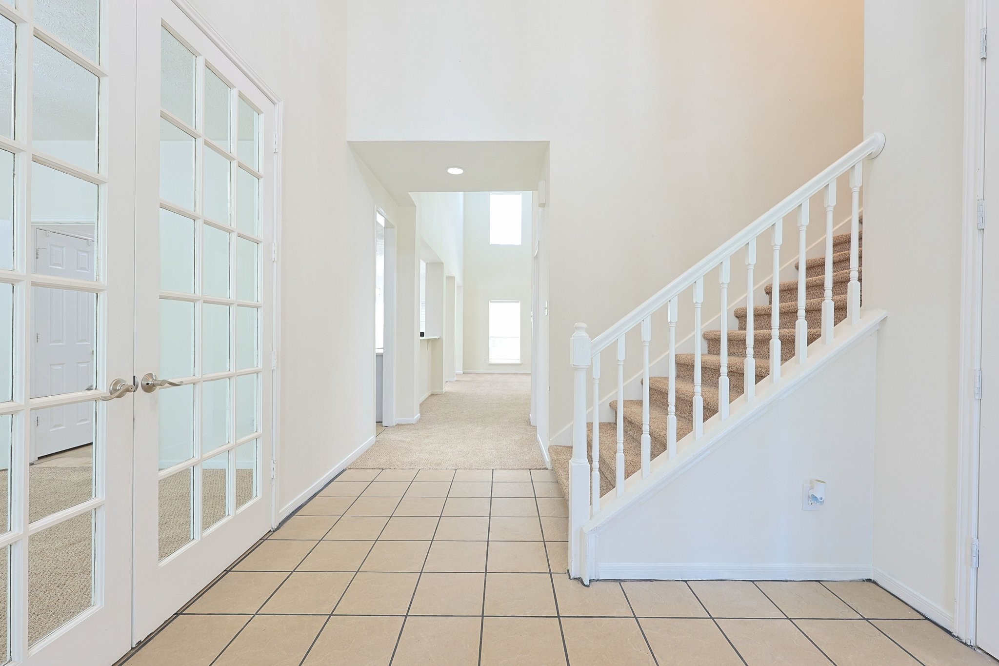 23019 Eastgate Village Drive Spring, TX 77373 - Photo 6 of 46 Bright and welcoming entryway featuring a tiled floor, French doors leading to a Dining and Study, and a carpeted staircase with a white banister on the right. The hallway extends to a well-lit area with high ceilings.