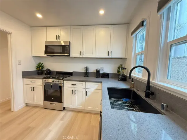 a kitchen with stainless steel appliances granite countertop a stove a sink a refrigerator and white cabinets with wooden floor