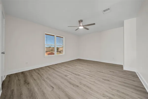 an empty room with wooden floor ceiling fan and window