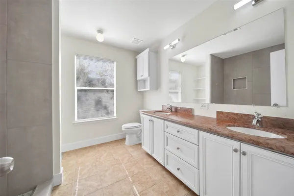 a spacious bathroom with a granite countertop sink a toilet a mirror and a window