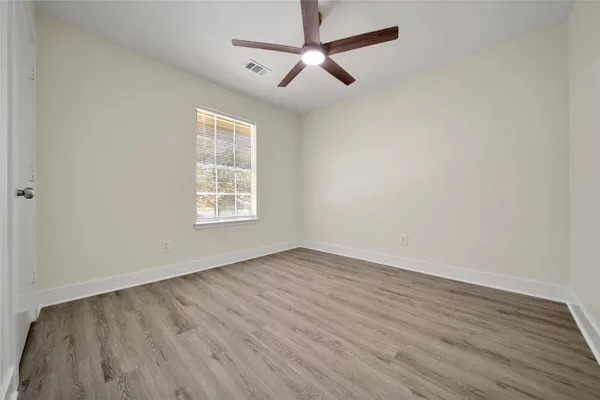 an empty room with wooden floor ceiling fan and windows