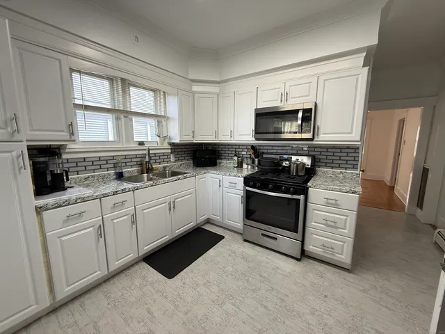 a kitchen with white cabinets white appliances and a window