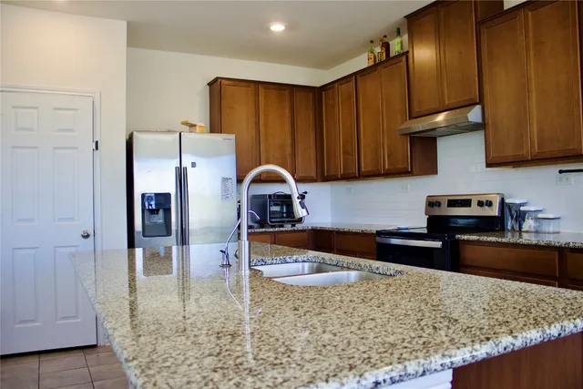 a kitchen with stainless steel appliances granite countertop a refrigerator a stove and a sink
