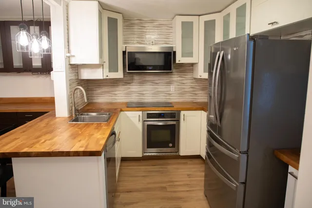 a kitchen with stainless steel appliances granite countertop a refrigerator a stove a sink dishwasher and white cabinets with wooden floor