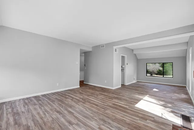 a view of an empty room with window and wooden floor