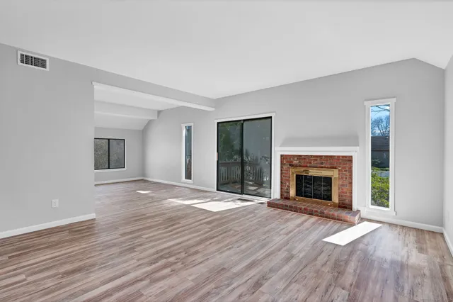 an empty room with wooden floor fireplace and windows