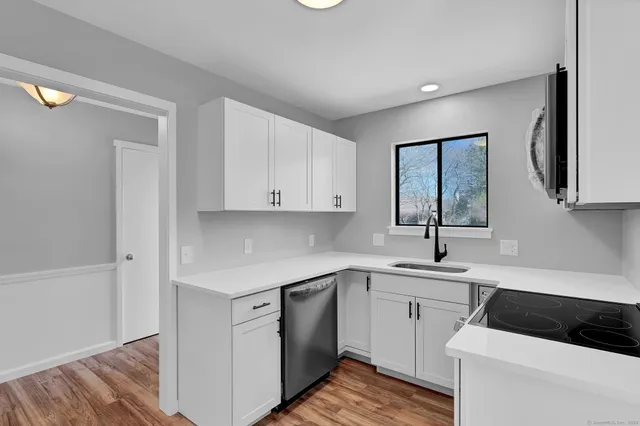 a kitchen with a sink dishwasher and white cabinets with wooden floor