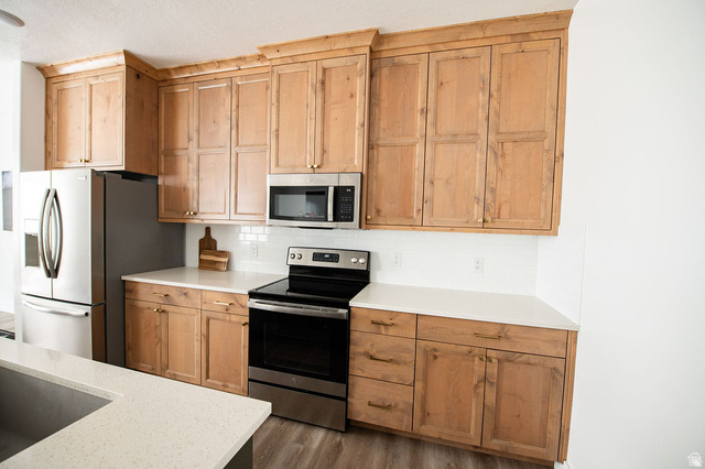 384 Ropelato Drive Nibley, UT 84321 - Photo 4 of 25 Light-finish wood cabinetry with gold-tone hardware, white countertops, stainless steel appliances, and white subway tile backsplash