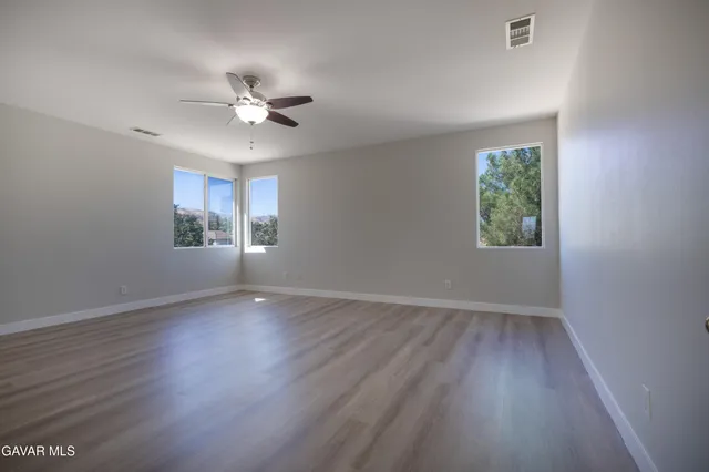 a view of an empty room with wooden floor and a ceiling fan