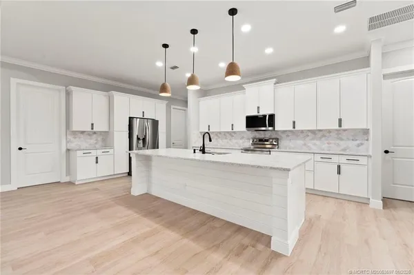 a large kitchen with stainless steel appliances kitchen island granite countertop a stove a sink and white cabinets with wooden floor
