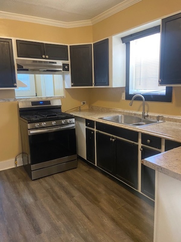 214 South Hackberry Avenue Luling, TX 78648 - Photo 17 of 22 Kitchen featuring gas range, crown molding, dark wood finished floors, light countertops, and under cabinet range hood