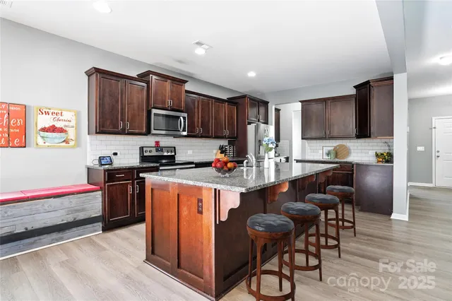 a kitchen with stainless steel appliances granite countertop a stove top oven a sink dishwasher and a refrigerator with wooden cabinets