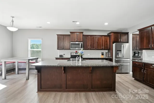 a kitchen with stainless steel appliances granite countertop wooden cabinets a sink dishwasher a stove and a refrigerator with wooden floor