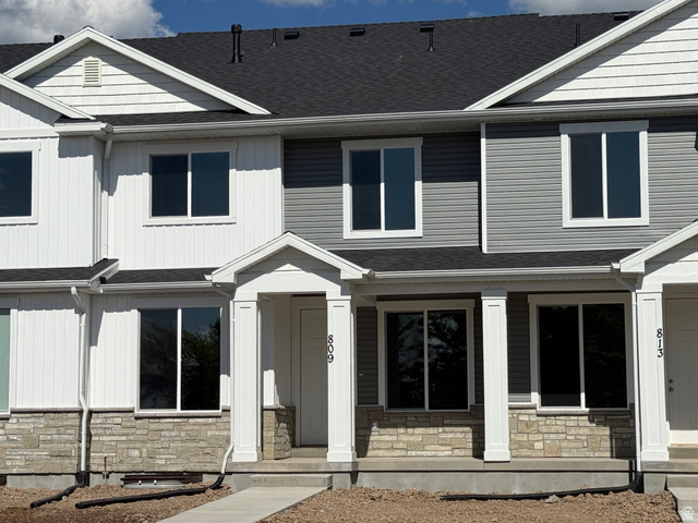 809 South 270th Street East, Unit 2 Smithfield, UT 84335 - Photo 2 of 23 Contemporary townhome exterior featuring a stone accent foundation, horizontal and vertical siding, a covered entry porch with columns, and a dark shingle roof