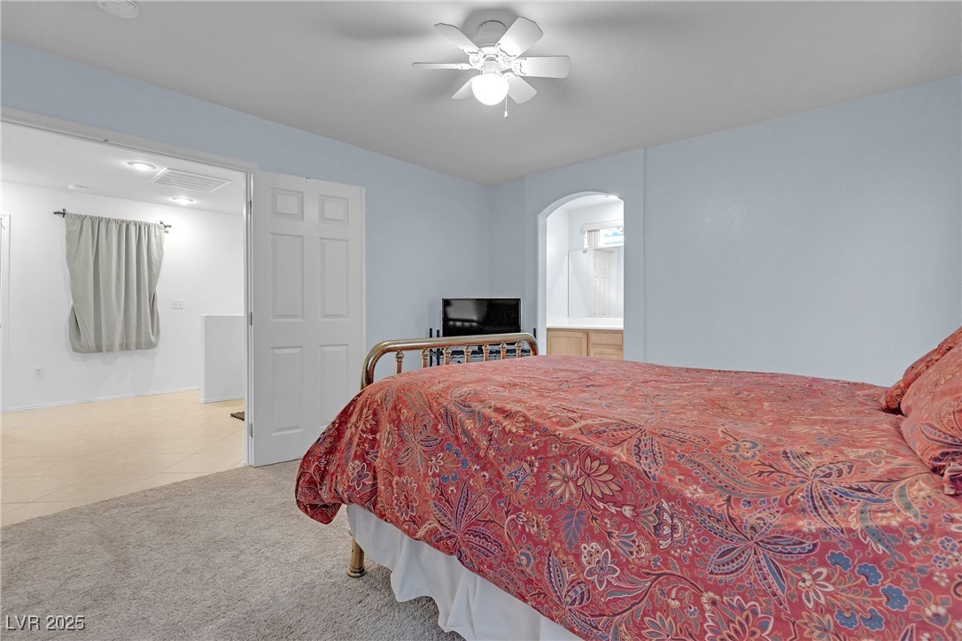 9065 Starling Wing Place Las Vegas, NV 89143 - Photo 26 of 53 Bedroom with light tile patterned floors, light colored carpet, connected bathroom, arched walkways, and ceiling fan