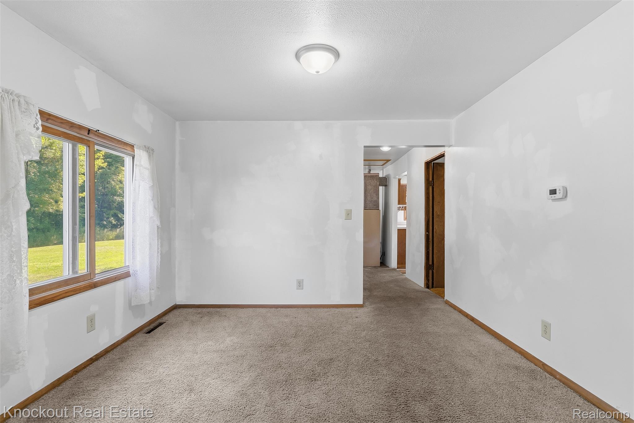 12845 Bueche Road Burt, MI 48417 - Photo 11 of 28 Carpeted room featuring a large window with wood trim, offering a view of a grassy area and mature trees