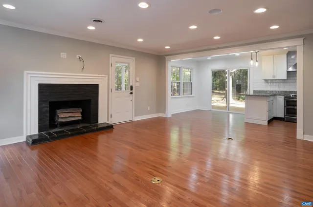 a view of an empty room with wooden floor fireplace and a window