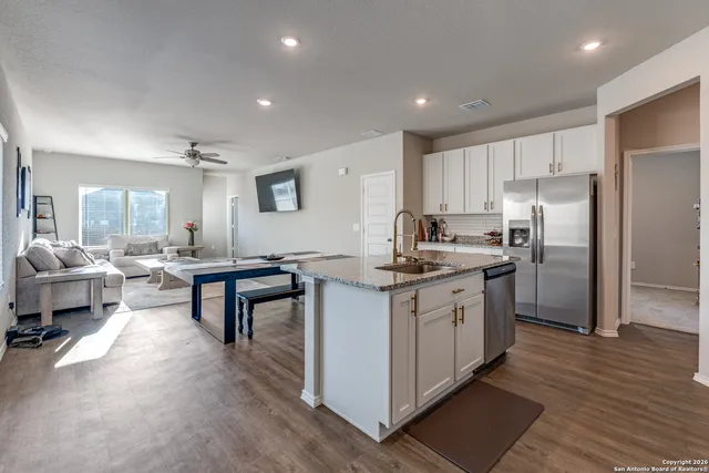 a kitchen with stainless steel appliances kitchen island granite countertop a refrigerator a stove a sink and a dining table with wooden floor