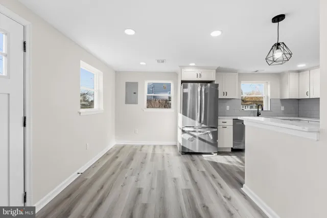 a kitchen with stainless steel appliances granite countertop a refrigerator a microwave oven a sink dishwasher and white cabinets with wooden floor