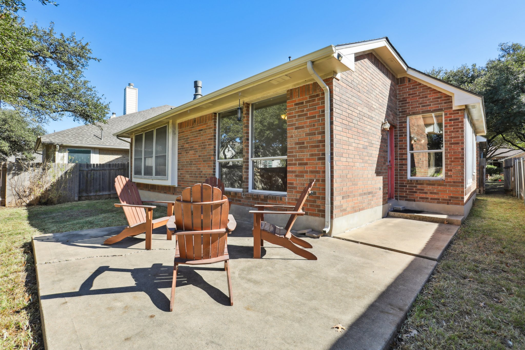 13541 Anarosa Loop Austin, TX 78727 - Photo 23 of 27 Expansive concrete patio with a brick exterior, multiple windows, and a red door