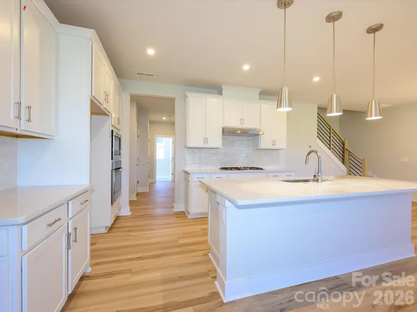 a view of a kitchen with kitchen island a sink wooden floor and a view of living room