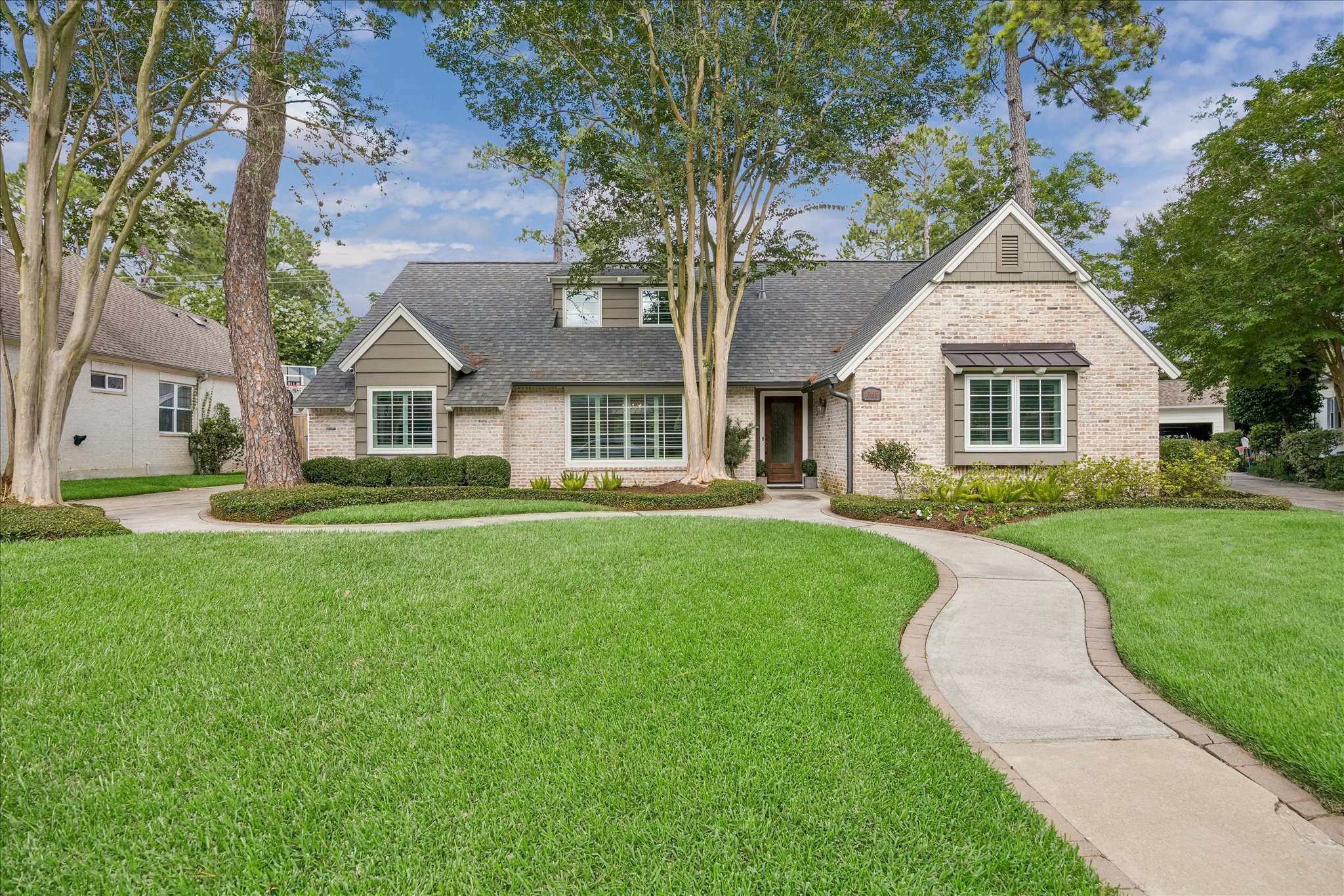 Charming single-story home in the heart of Fonn Villas with a brick exterior and gabled roof, set amidst a lush green lawn. It is flanked by mature trees and well-maintained landscaping.