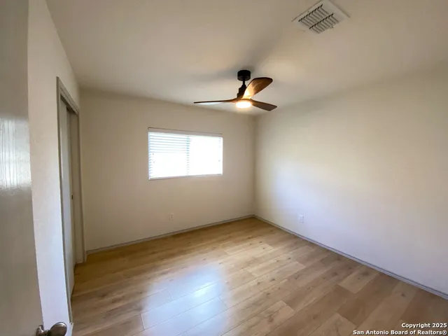 an empty room with wooden floor fan and windows