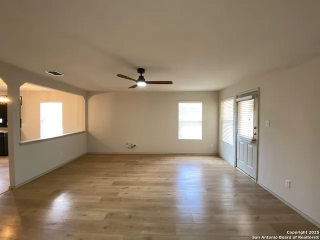 an empty room with wooden floor fan and windows