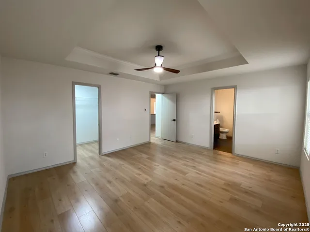 a view of an empty room with wooden floor and a ceiling fan