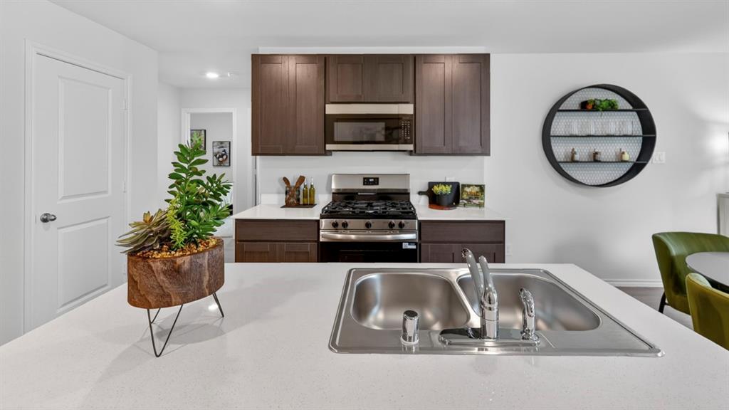 3514 Spring Time Street Terrell, TX 75126 - Photo 7 of 26 Kitchen island with an undermount double basin stainless steel sink, stainless steel faucet, and white countertop