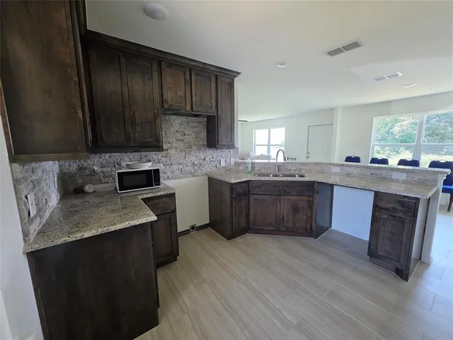 a kitchen with stainless steel appliances granite countertop wooden cabinets a sink a stove a refrigerator and island with wooden floor