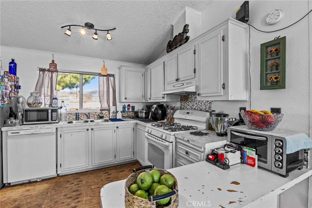 33945 Red Mountain Road Hemet, CA 92544 - Photo 26 of 30 a kitchen with white cabinets a sink dishwasher and a fireplace with wooden floor