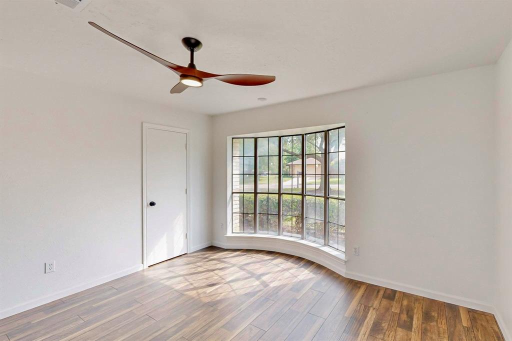 3965 Singleleaf Lane Fort Worth, TX 76133 - Photo 27 of 39 Room featuring a curved bay window with grid-patterned panes, wood-finish flooring, a modern ceiling fan with integrated lighting, a white door with a black handle, and white baseboards