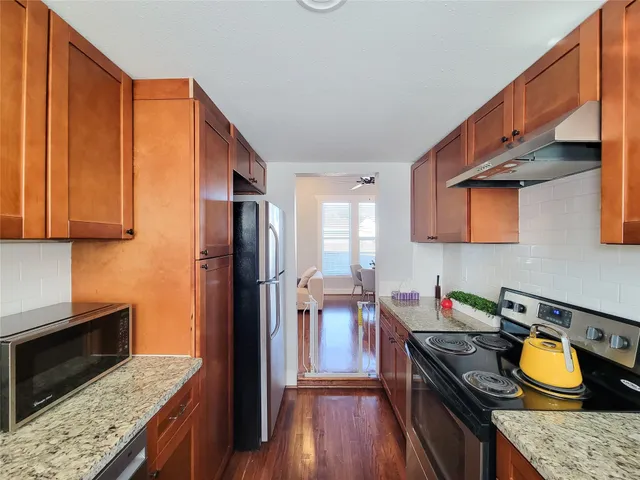 a kitchen with granite countertop wooden cabinets a sink and dishwasher stove with wooden floor