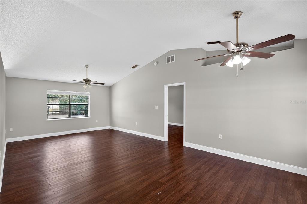 2737 East Dorchester Drive Deltona, FL 32738 - Photo 11 of 32 an empty room with wooden floor chandelier fan and windows