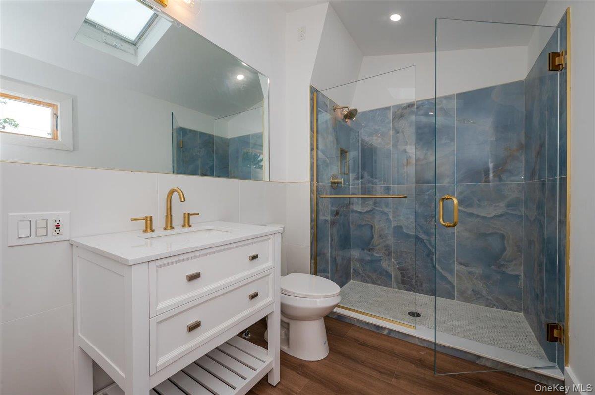 56 Oak Beach Road Babylon, NY 11702 - Photo 23 of 30 Fully renovated first floor bathroom with porcelain wall tiles, 3/8 Starphire glass shower enclosure, with gold finishes and luxury vinyl flooring