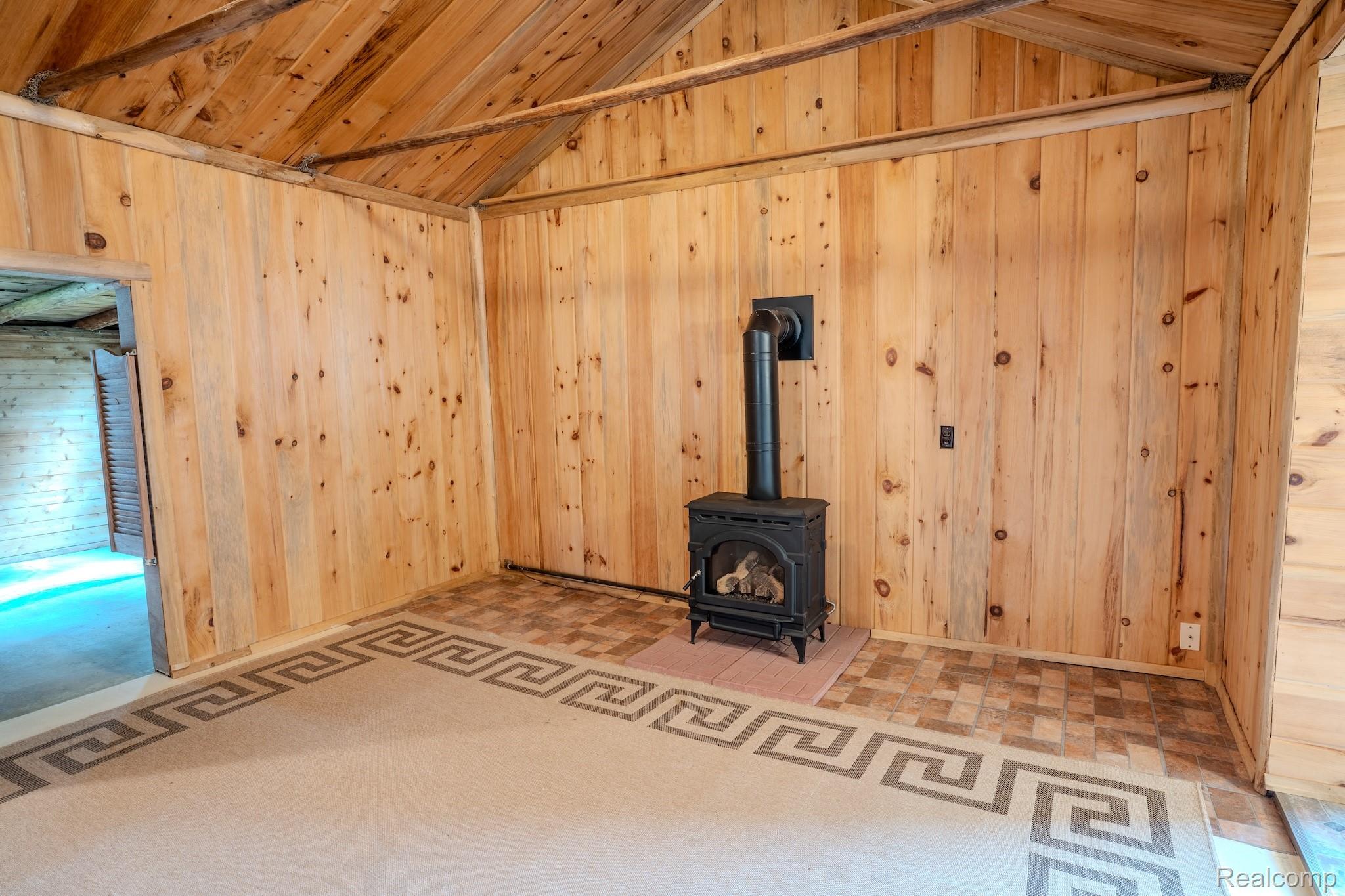 4350 Shrew Road Lincoln, MI 48742 - Photo 14 of 32 Interior room with natural wood paneling, exposed wood ceiling beams, and a black wood-burning stove