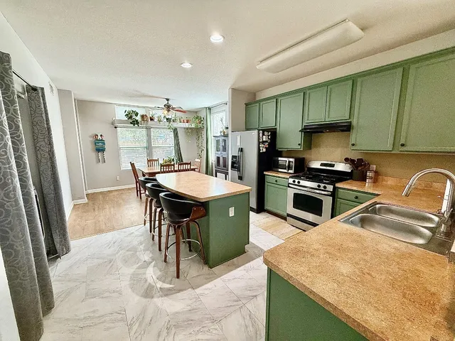 a kitchen with stainless steel appliances kitchen island granite countertop a sink a stove a refrigerator cabinets and chairs