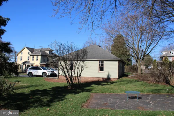 a view of a white house in front of a big yard plants and large trees