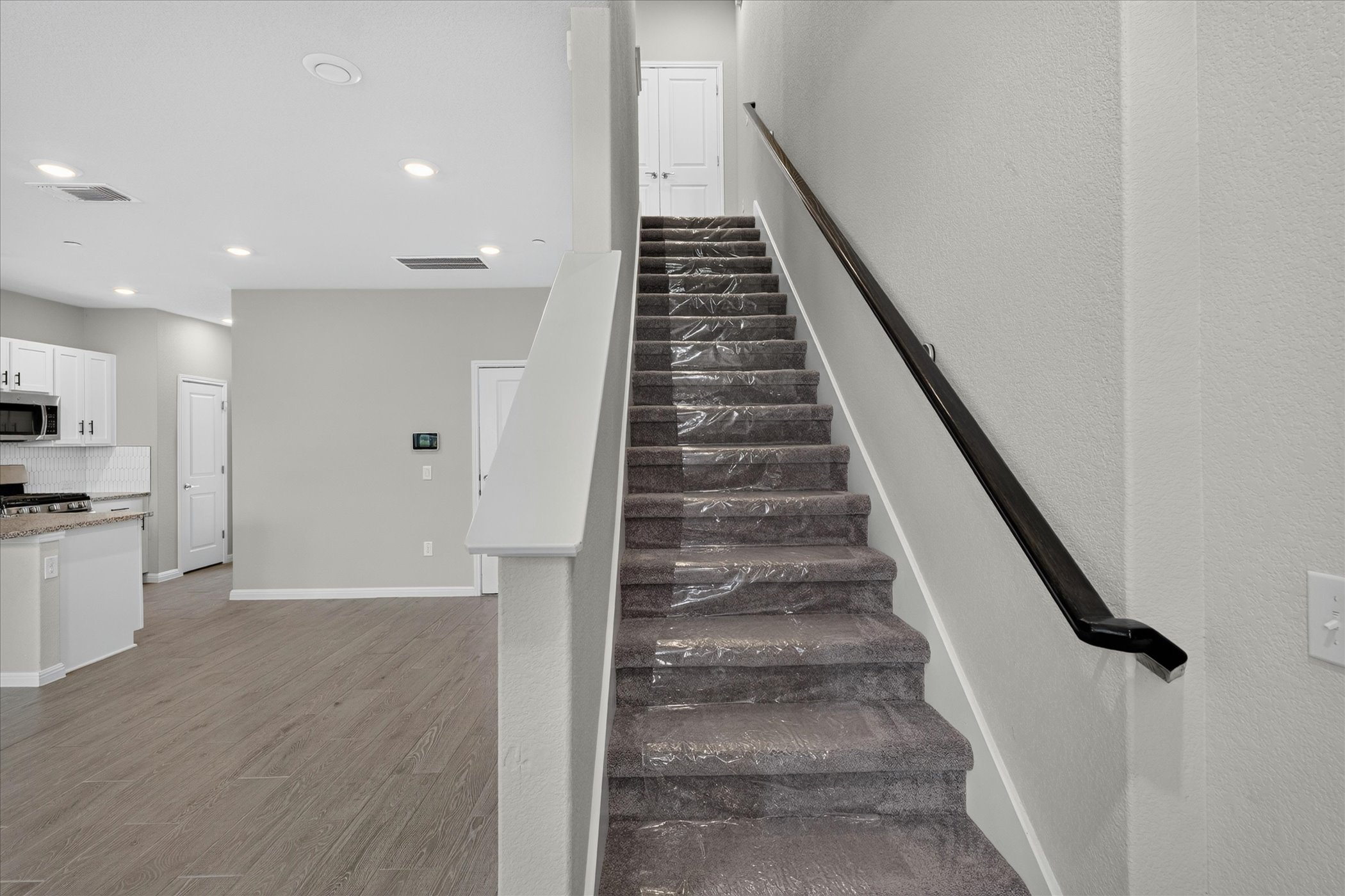 9015 Cattle Baron Path, Unit 1102 Austin, TX 78747 - Photo 10 of 25 A grand staircase with dark wood railing and a sun-drenched, open-concept living area with plank flooring.
