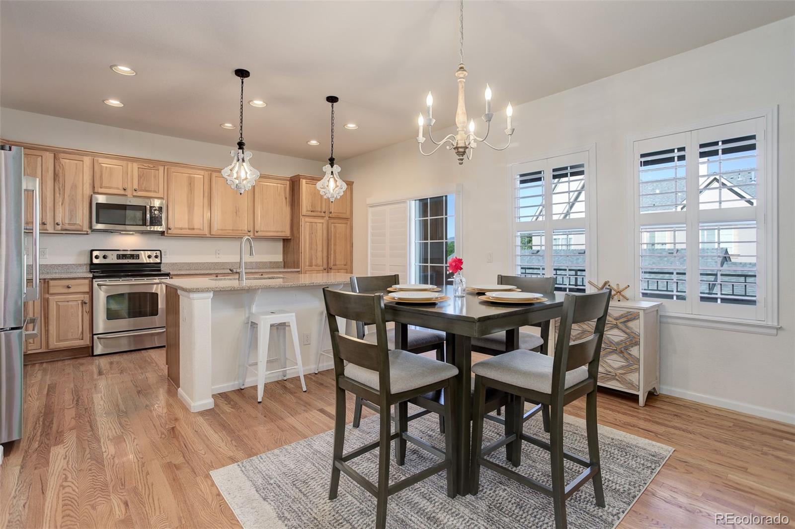 674 Bristle Pine Circle, Unit D Highlands Ranch, CO 80129 - Photo 5 of 31 a kitchen with stainless steel appliances granite countertop a stove a refrigerator a kitchen island a dining table and chairs with wooden floor